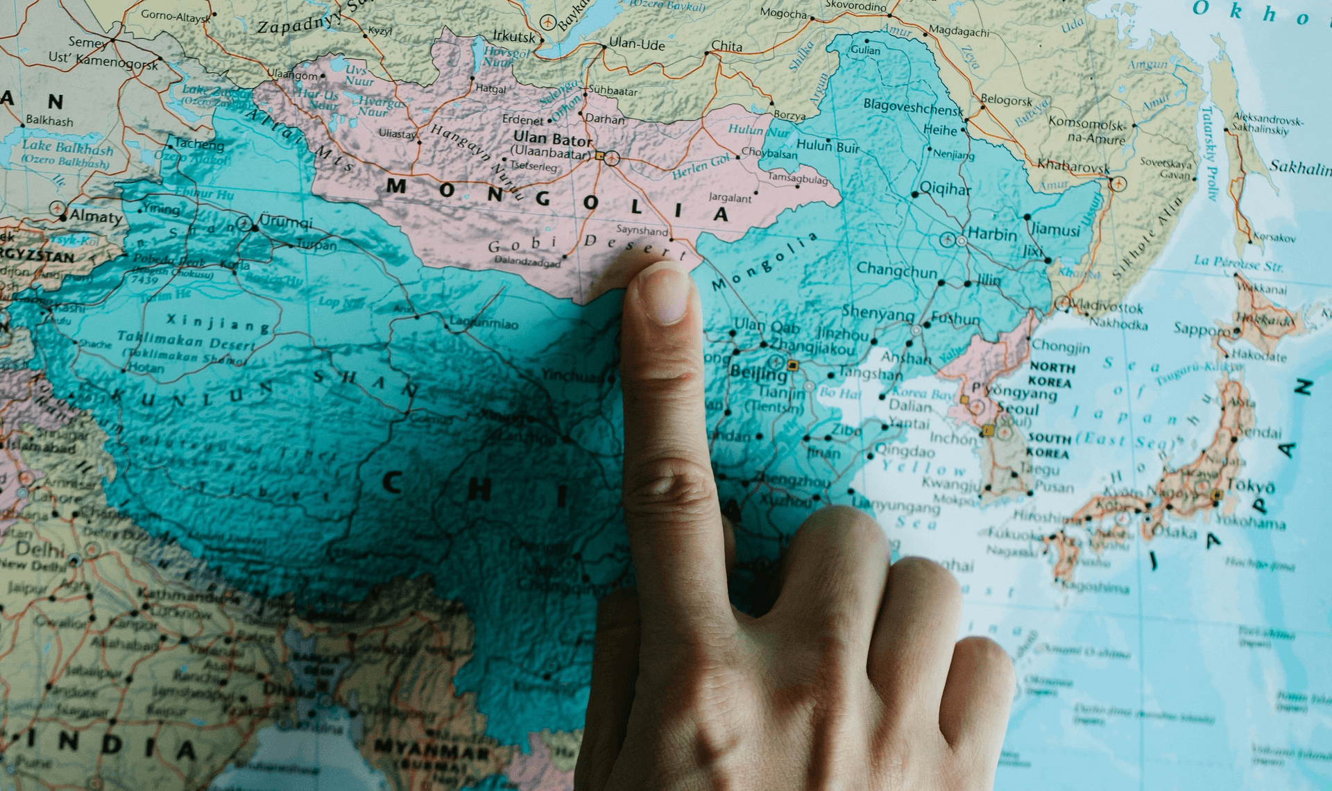 A finger pointing at Mongolia on a map